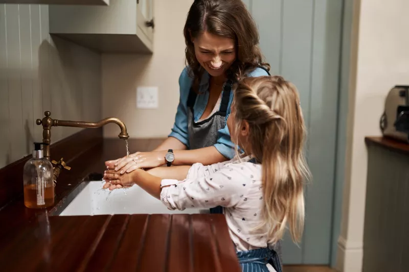 A mother and daughter wash their hands at the kitchen sink.