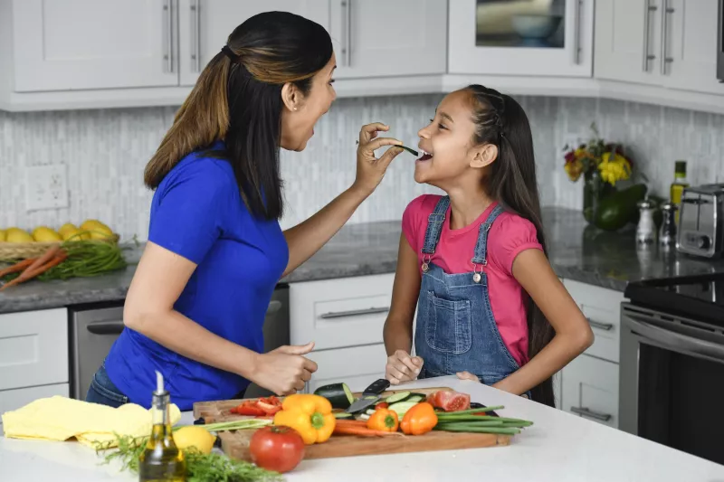 A mother and daughter snacking on vegetables.