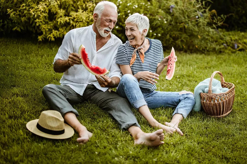 A couple eating watermelon at an outdoor picnic.