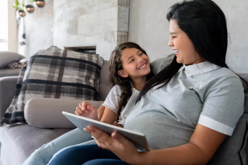 A pregnant mother and her daughter on the couch.