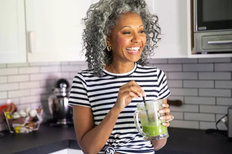 A woman drinking a healthy green smoothie in her kitchen.