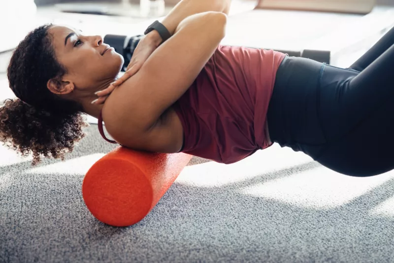 A woman foam rolling her upper back.