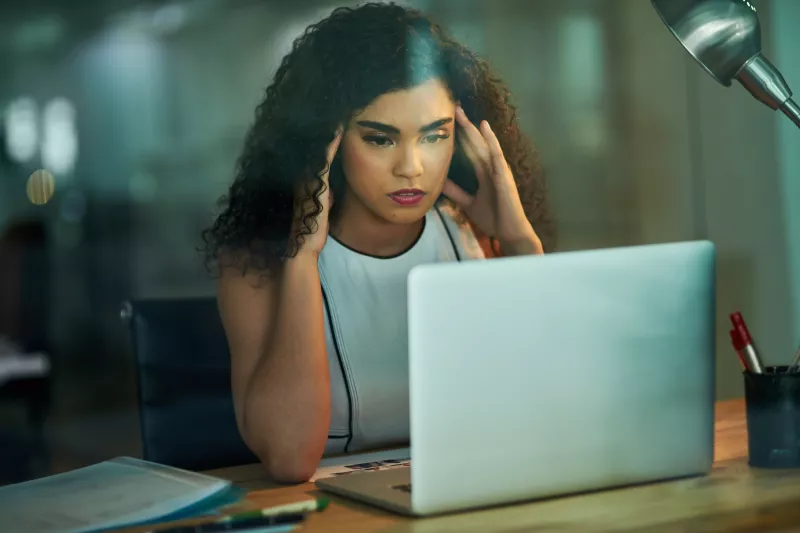 A woman massaging her temples at her desk at work.