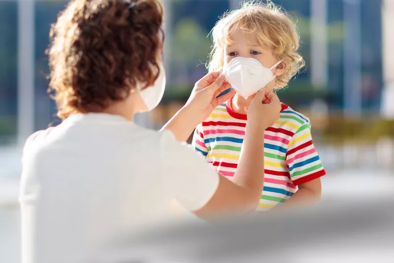 A mom helps her son position his face mask.