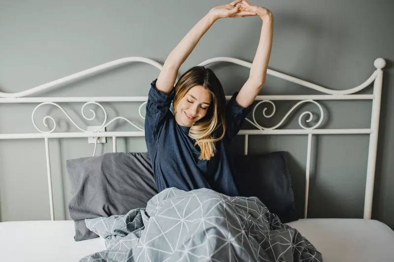 A woman stretching in bed after a good night's sleep.