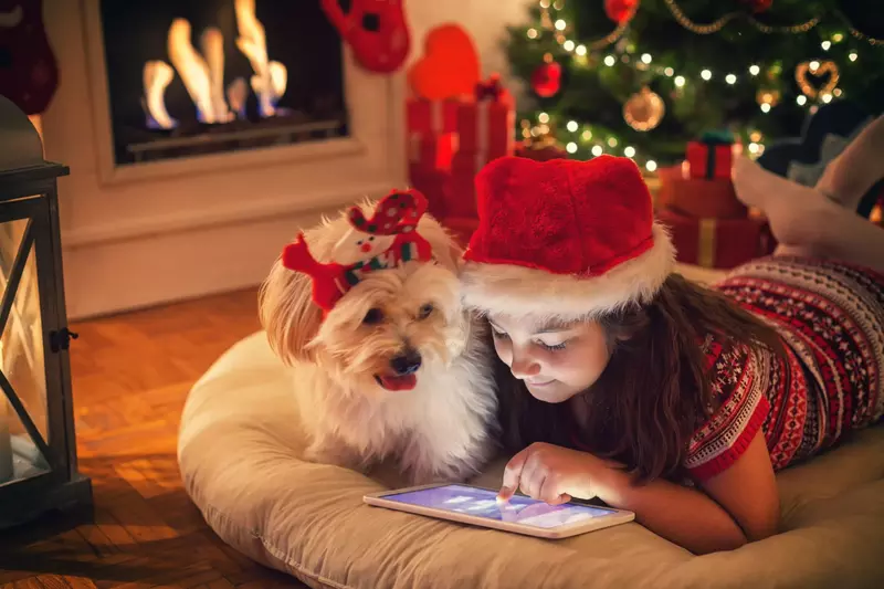 Young girl playing on tablet with dog next to her during the holidays