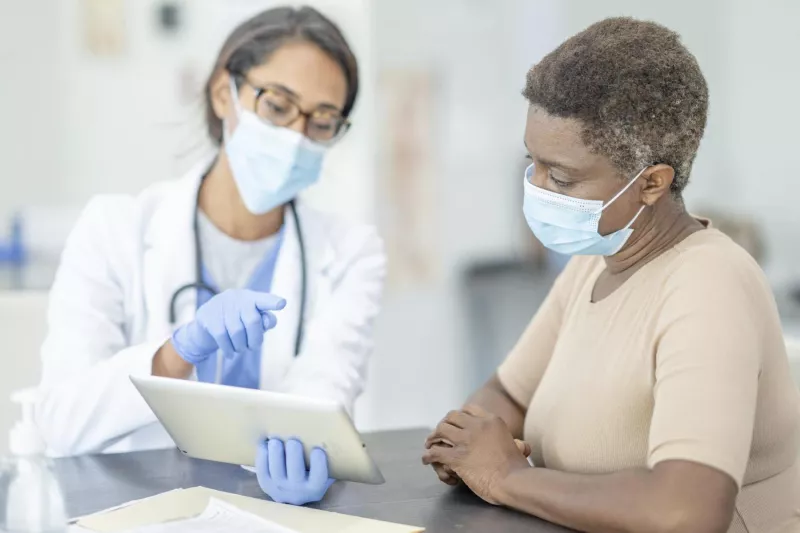 Older black woman talking with female doctor wearing masks