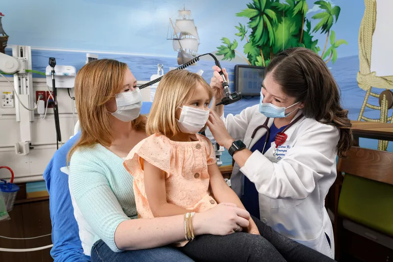 Dr. Kirby checking the ear of a pediatric patient while she sits on her mother's lap.