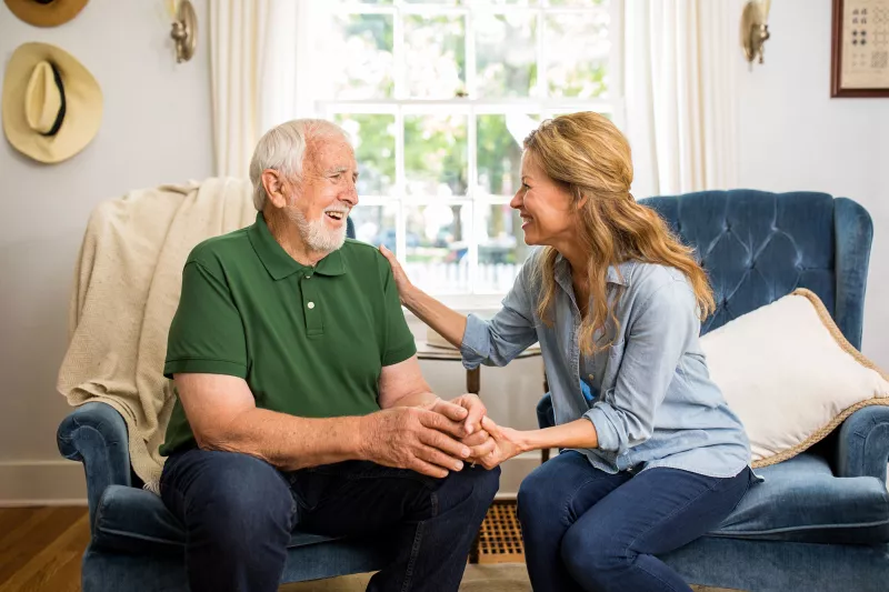 A daughter having a conversation with her elderly father in the family room.