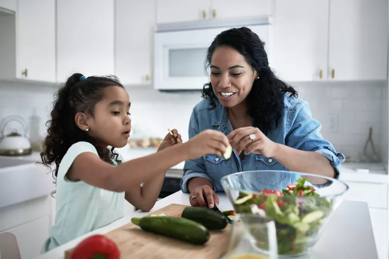 A mother and daughter prepare a salad at home.