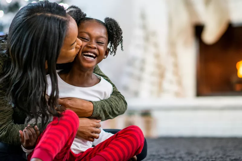 A mother hugging her daughter in front of the fireplace.