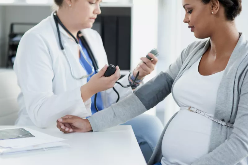 One pregnant woman getting her blood checked by a female doctor in scrubs.