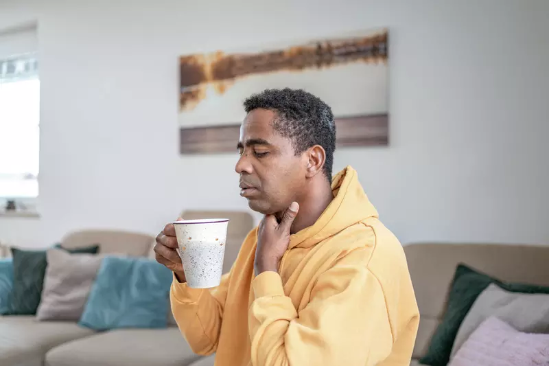 A man with a sore throat sips a cup of hot tea.