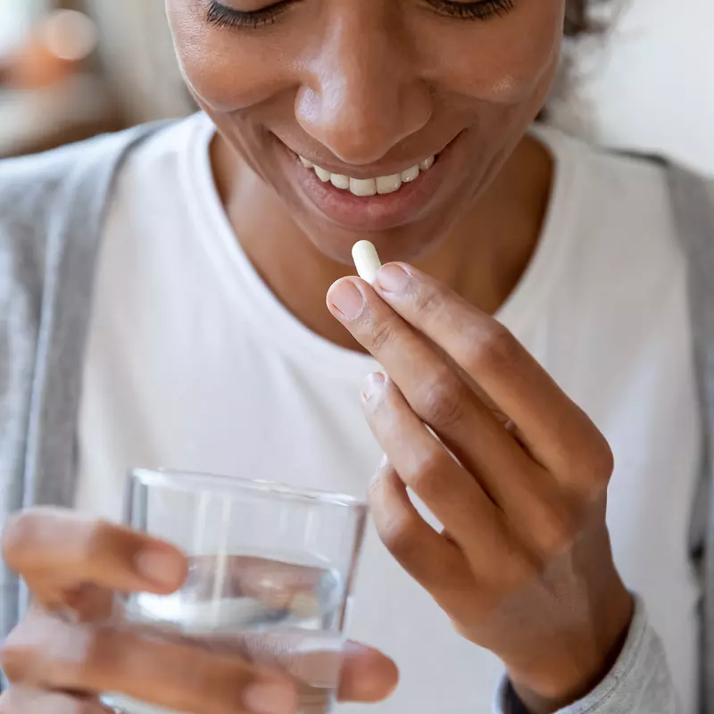A woman smiles as she's about to take a vitamin.