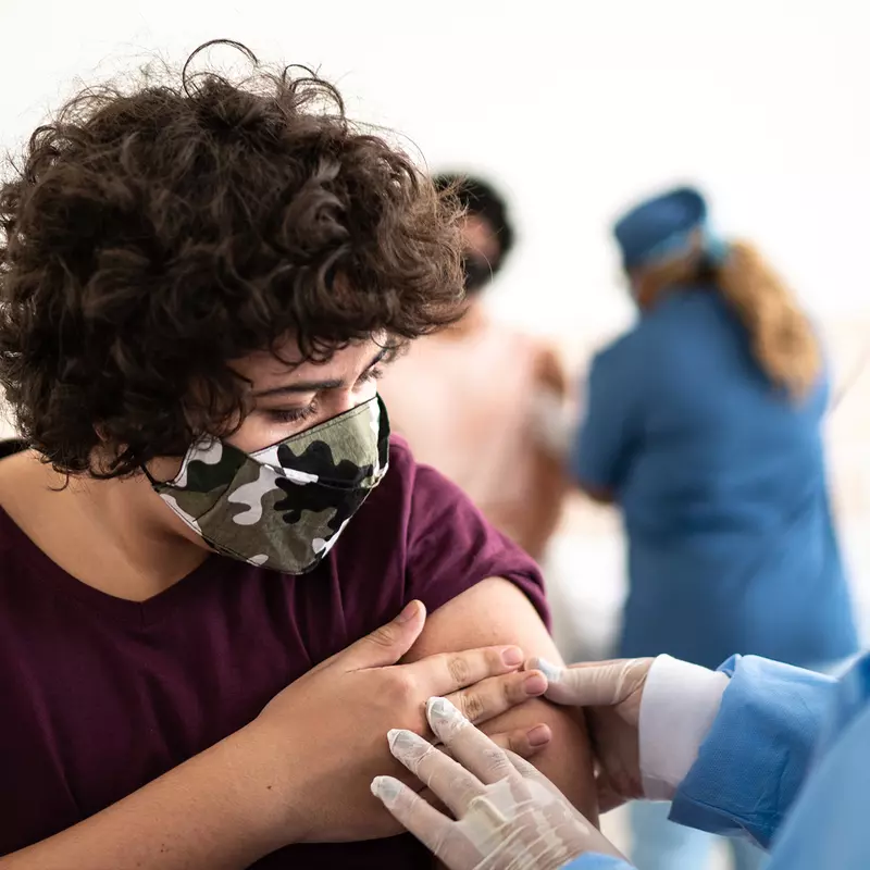 Woman wearing a mask get's a flu shot from a medical professional in blue scrubs