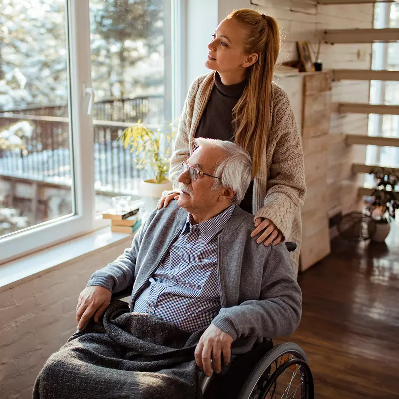 Caregiver Looks Out the Window with a Senior Patient at the Newly Fallen Snow.
