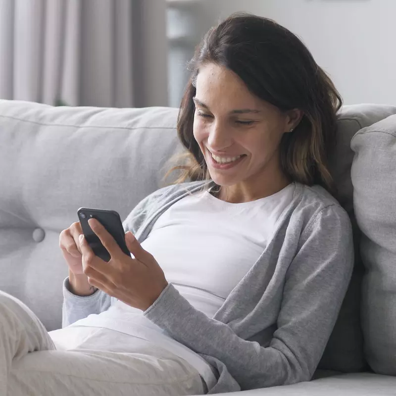A Woman Sits on Her Couch and Uses Her Smartphone.