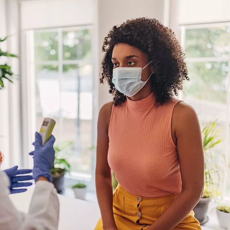 A Woman Wearing a Face Mask has her Temperature Taken by a Care Provider