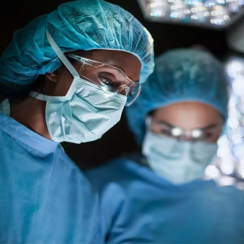 Surgeons Wearing Full Scrubs and Masks Operate on an Unseen Patient
