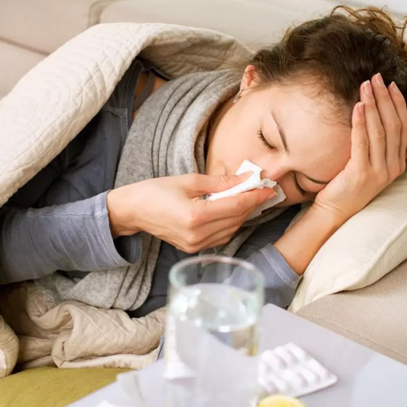 A woman laying in bed with the flu, water and medicine on her nightstand.