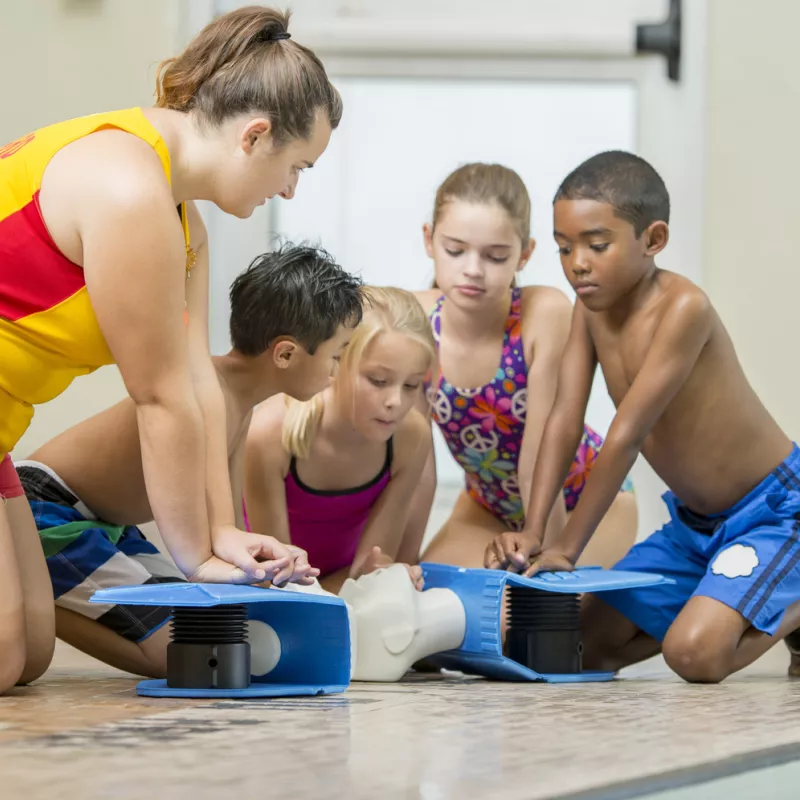 Four children learn CPR from an adult poolside.