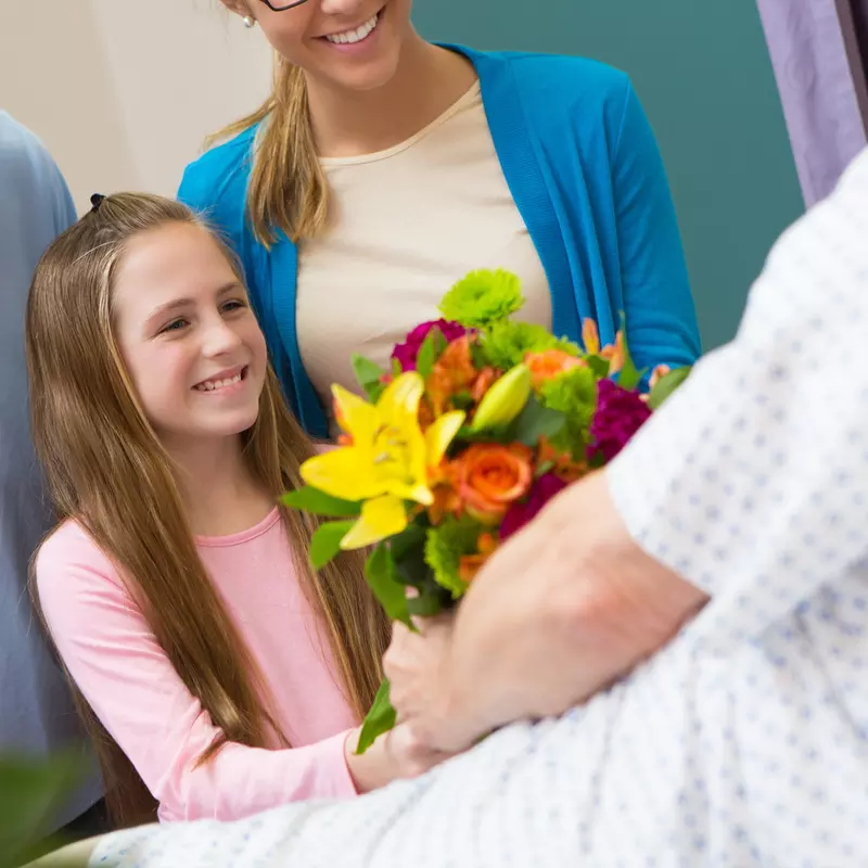 Family with child giving flowers to a hospital patient