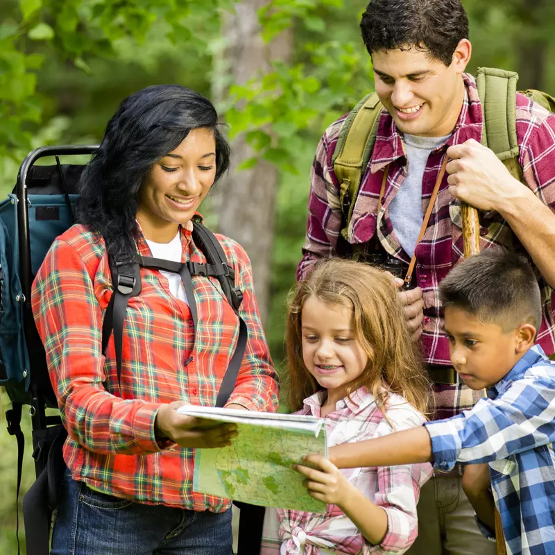 A family reads a map together while hiking in the woods.