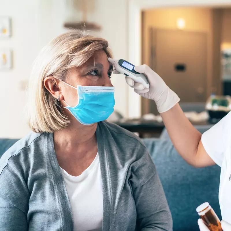 Doctor wearing a mask checking woman's temperature.