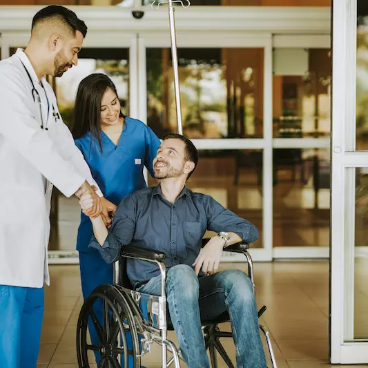 Doctor shaking hands with man as he leaves hospital in a wheelchair