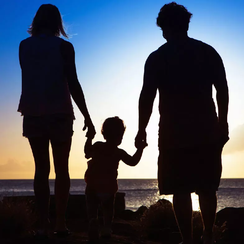 A silhouette of a mother, father, and their child looking at the ocean.