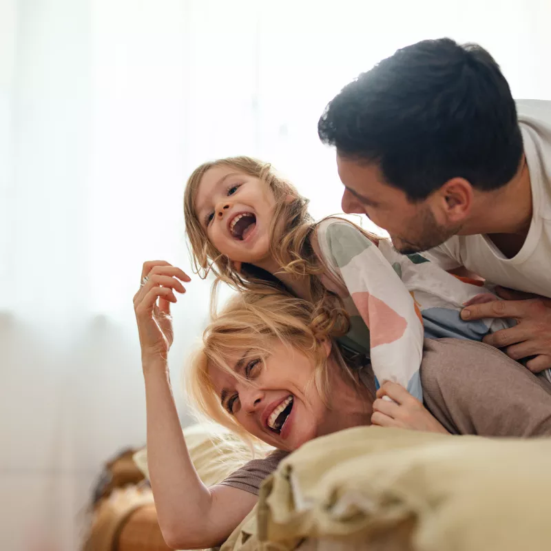 A family laughing while laying on a bed at home.