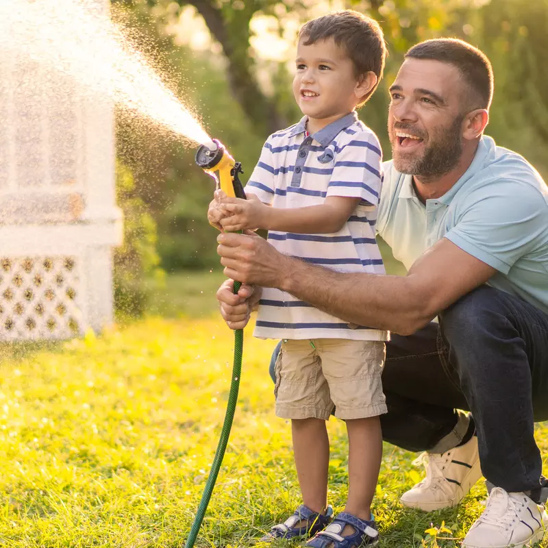 A Father and Son Spray a Garden Hose in the Front Yard as They Laugh