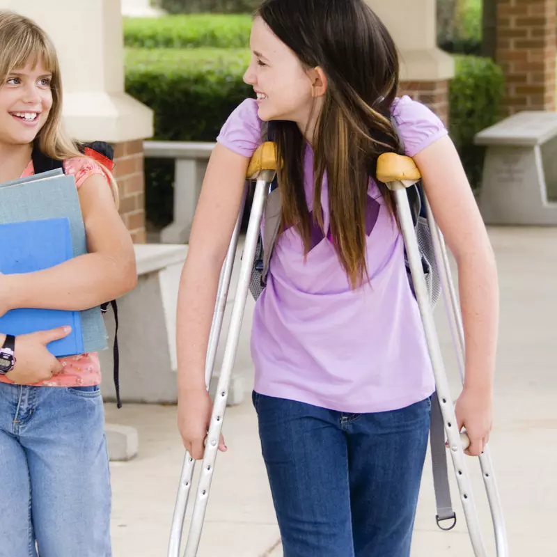 A girl on crutches walks with her friend at school