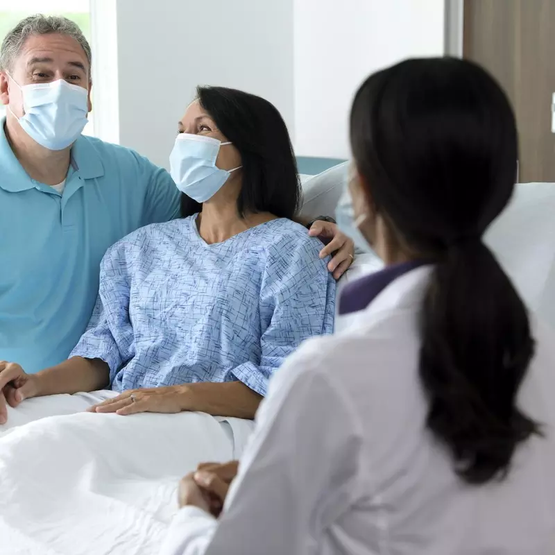 Couple in hospital room wearing masks talking to doctor