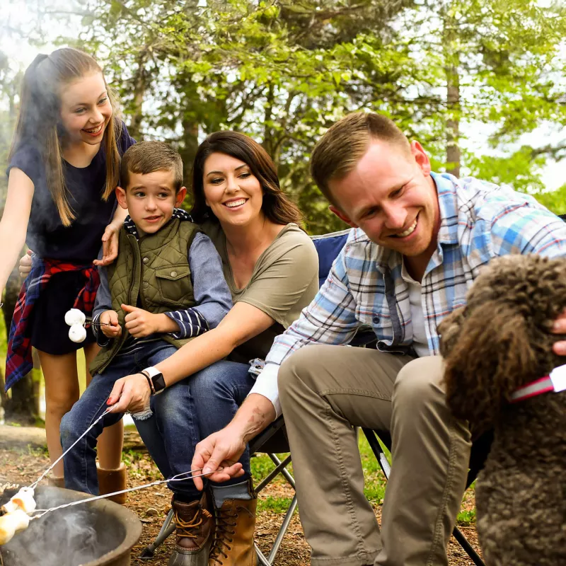 Family sitting around campfire and cooking s'mores with the family dog
