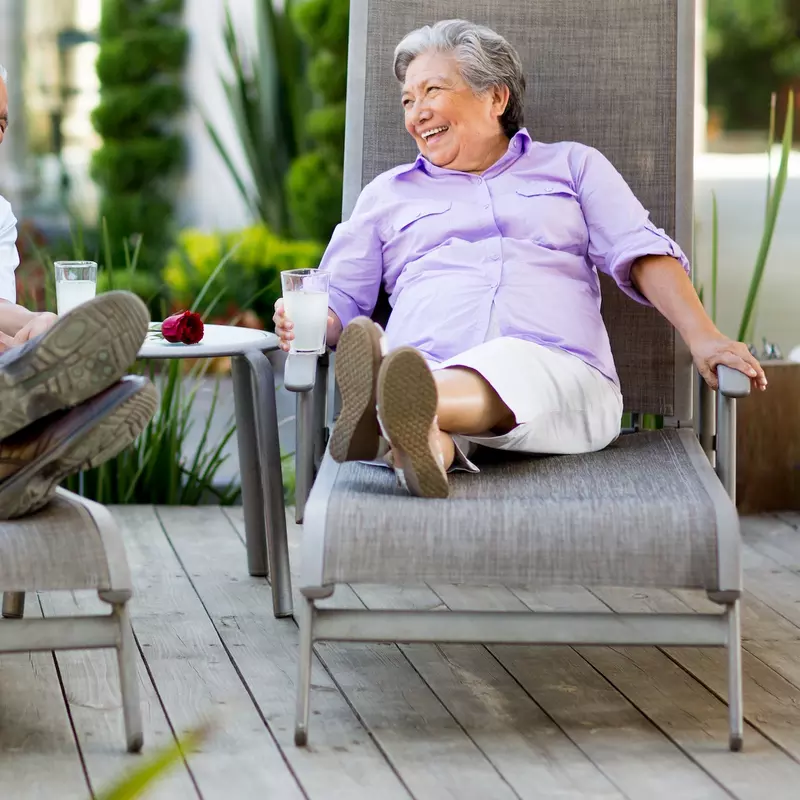A couple chatting and laughing in lounge chairs outdoors.