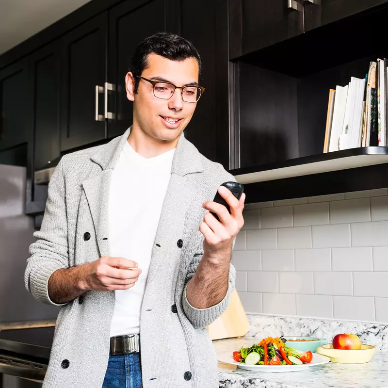 A Man Wearing Glasses Checks His Glucose Levels Before Eating a Healthy Meal in His Kitchen