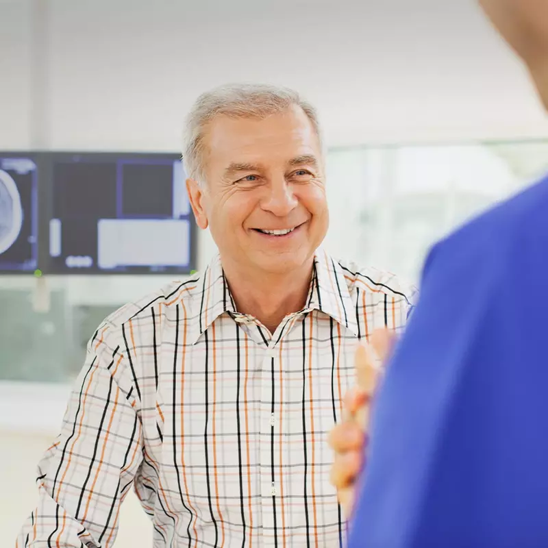 Man speaking with a doctor with imaging results on a screen behind him