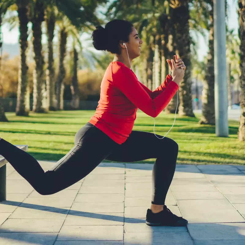 A woman doing a lunge outdoors on a bench.