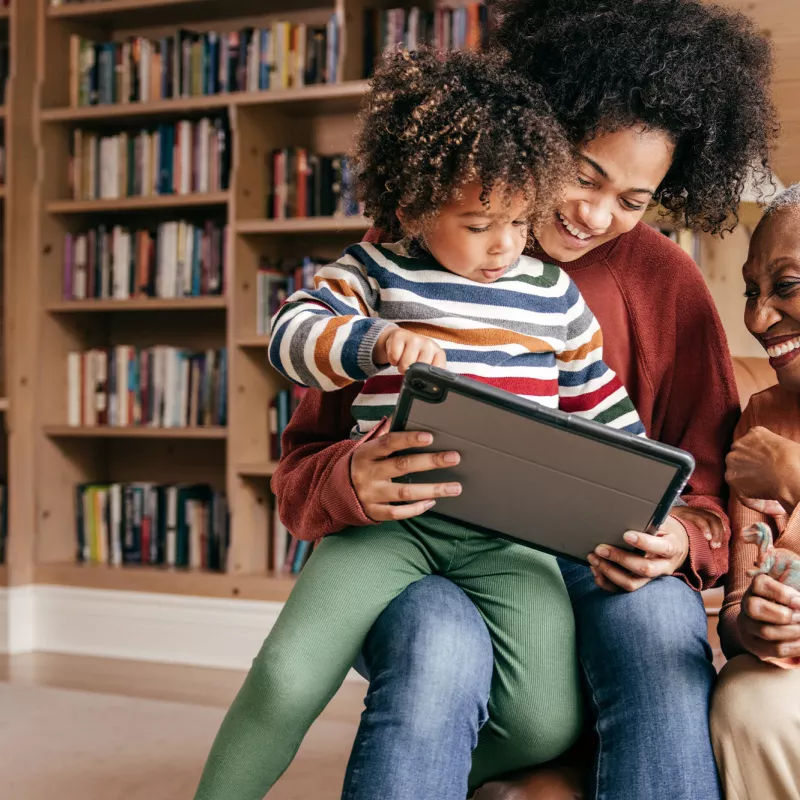 Mother, grandmother and child looking at a tablet at home.