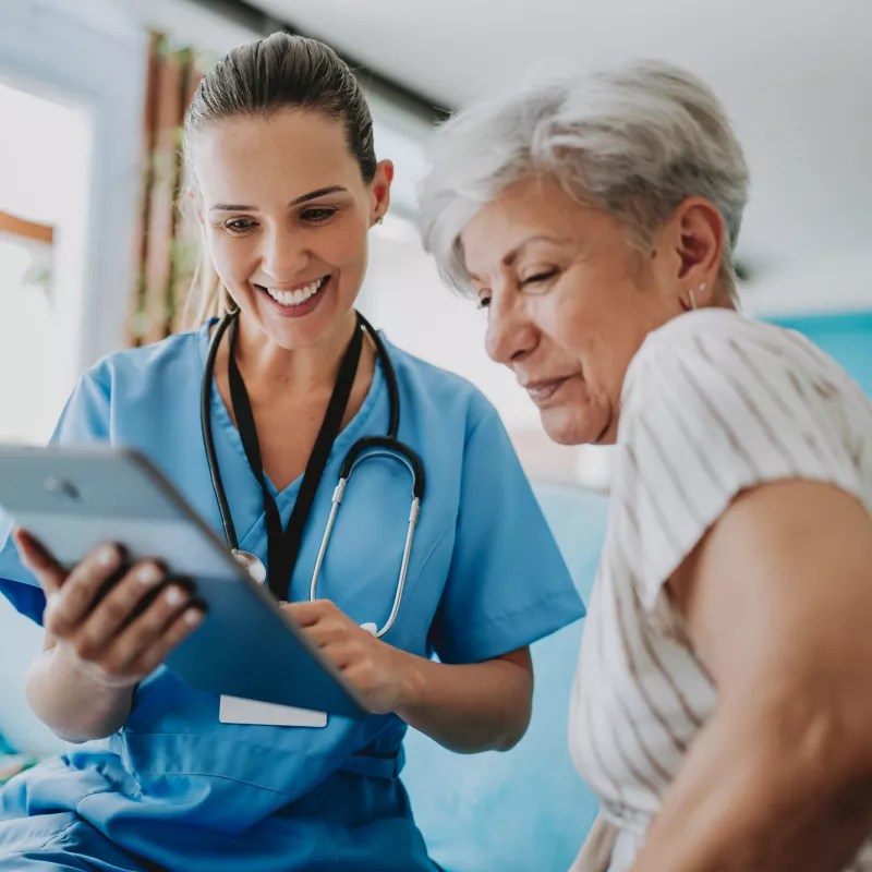 A female nurse showing an older woman patient information on a tablet.