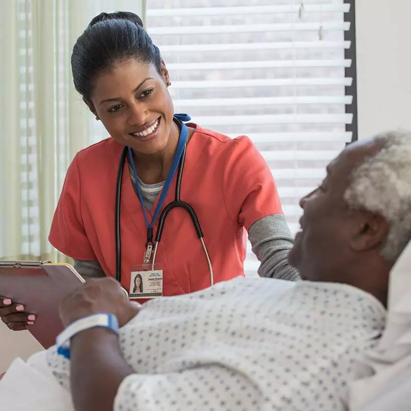 Nurse holding clipboard and standing by elderly patient's bedside