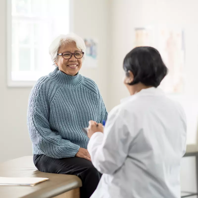 An older female patient talking to a female physician in an exam room.