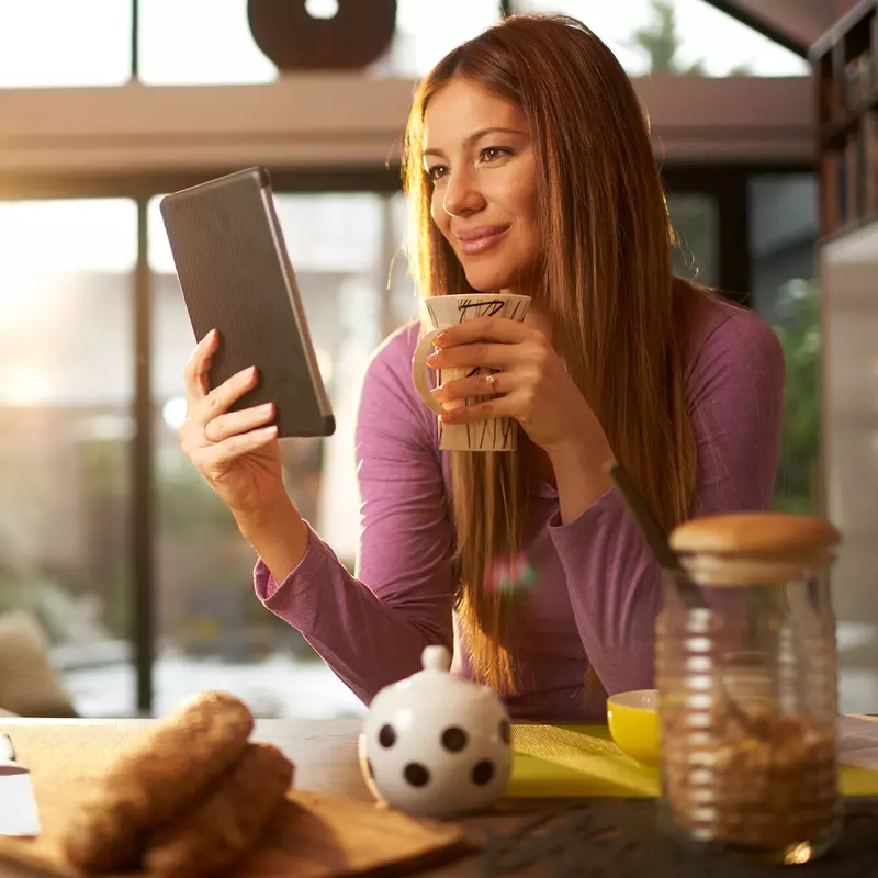 Woman drinking coffee in the morning while looking at her tablet.