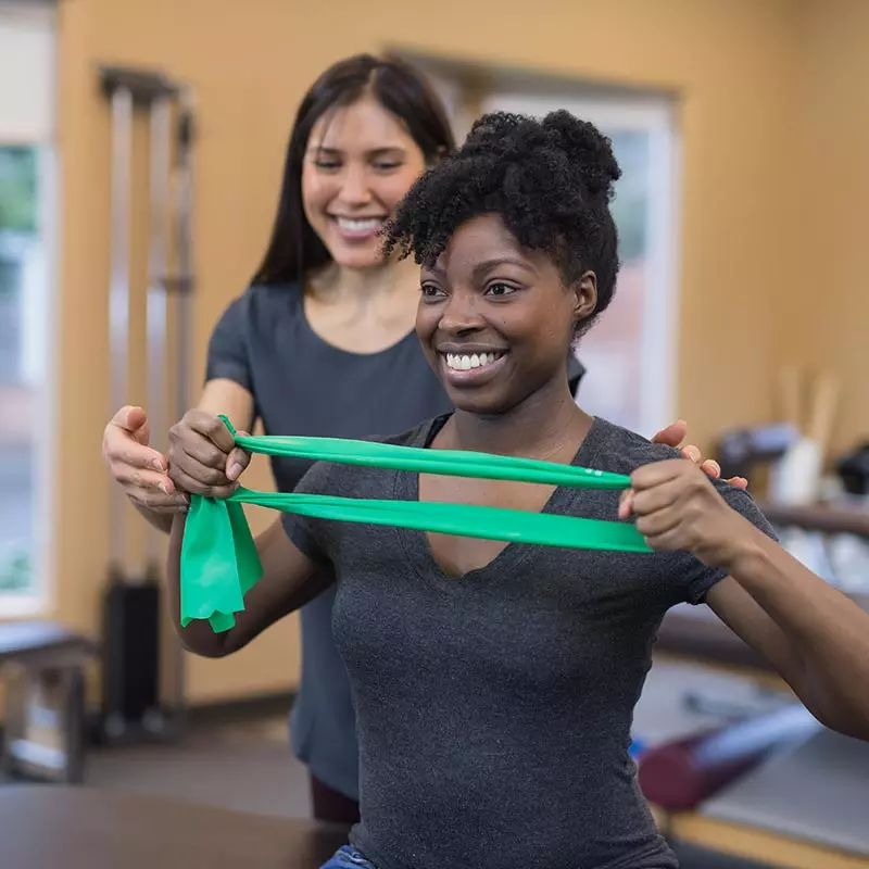 Woman stretching a resistance band with help from a rehab professional