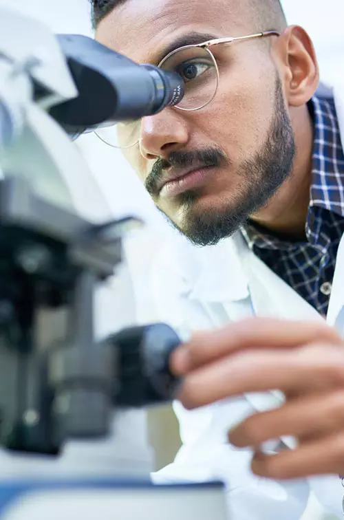 Man looking into a microscope to analyze the results of a clinical trial.