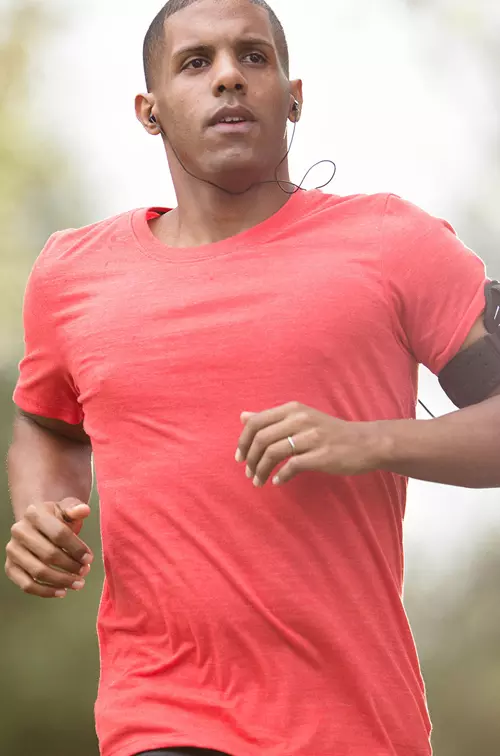 Man in a red shirt running outside while listening to music.