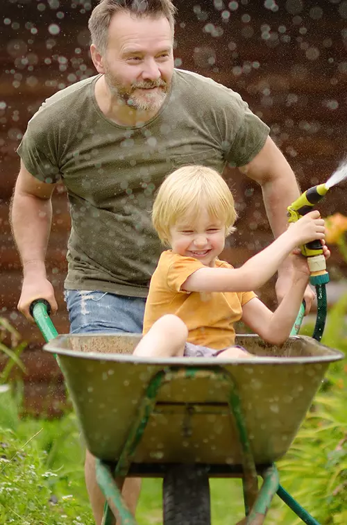 A Father and Son Spray a Garden Hose in the Front Yard as They Laugh