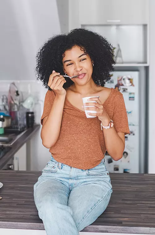 A woman sitting on her counter eating yogurt. 